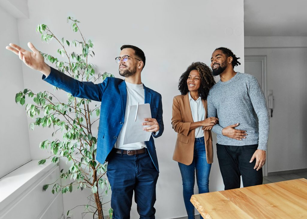 When is the Best Time to Buy a New Home? Young happy couple and an agent in a new property