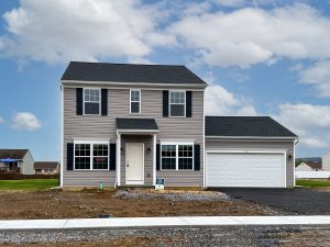 Two-story home with gray siding, black shutters, and a two-car garage in front of a partially finished driveway.