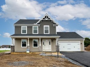 Two-story home with brown and gray siding, stone accents, and a two-car garage in front of an unfinished driveway.