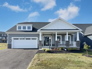 A single-story home with a gray exterior, white trim, and a covered front porch. The house has a two-car garage and stone accents.